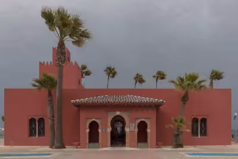 The red Bil-Bil castle on the seafront of Benalmádena, with horseshoe arches at its entrance and palm trees bending in the wind