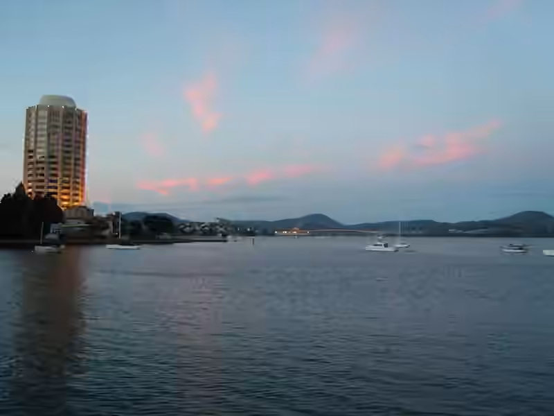 The Wrest Point hotel and casino tower lit at dusk on the shore of the River Derwent, with boats at anchor