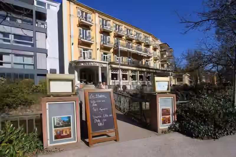 The Atlantic Parkhotel seen from the footbridge over the river Oos, with menu boards at the bridge and the hotel entrance behind