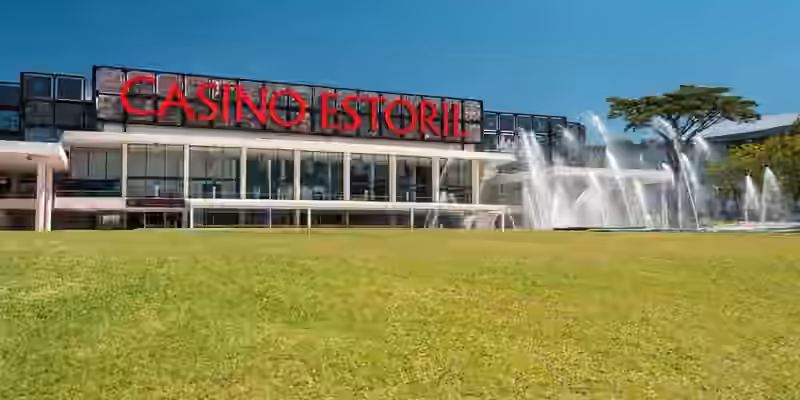 Casino Estoril seen across a lawn, with its red rooftop sign and fountains in front of the building