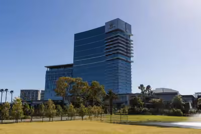 The glass tower of Crown Towers Perth with the Crown emblem at the top, seen across a lawn and trees in Burswood Park