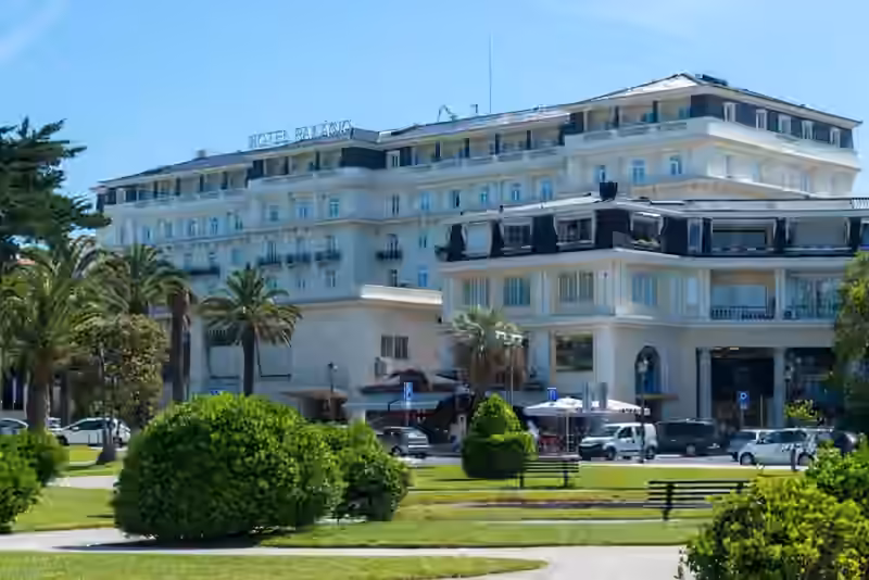Hotel Palácio Estoril with its rooftop sign, seen from the park, with palm trees and a lower building in front
