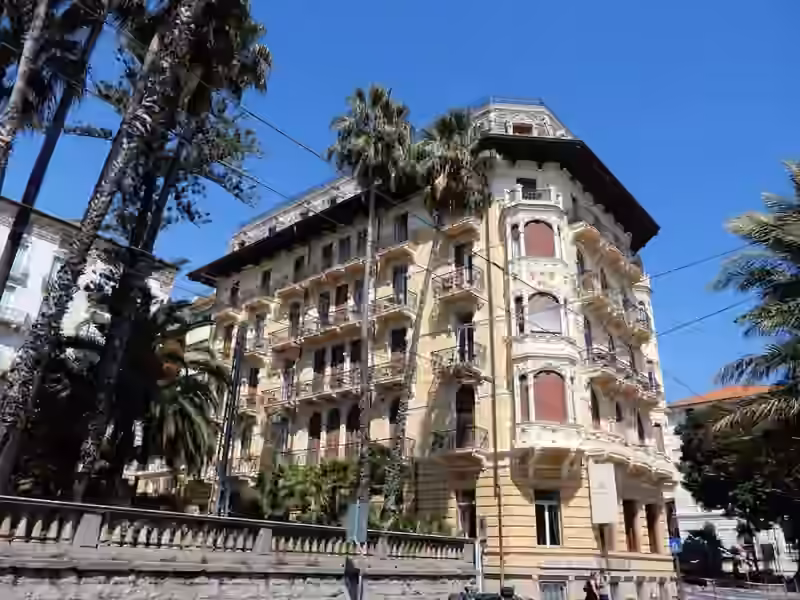 Palazzo Riviera, the yellow Art Nouveau building of the Lolli Palace Hotel, seen from the street behind palm trees