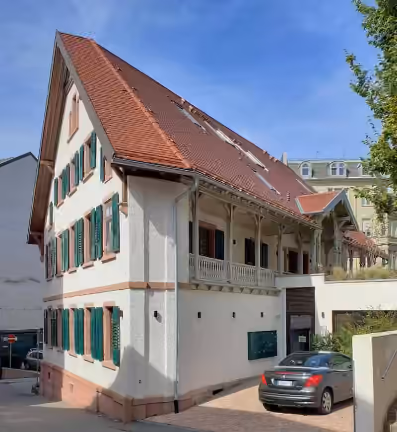 The house at Rettigstraße 1 in Baden-Baden, the annex of THE FLORIS, with white walls, green shutters and a wooden veranda