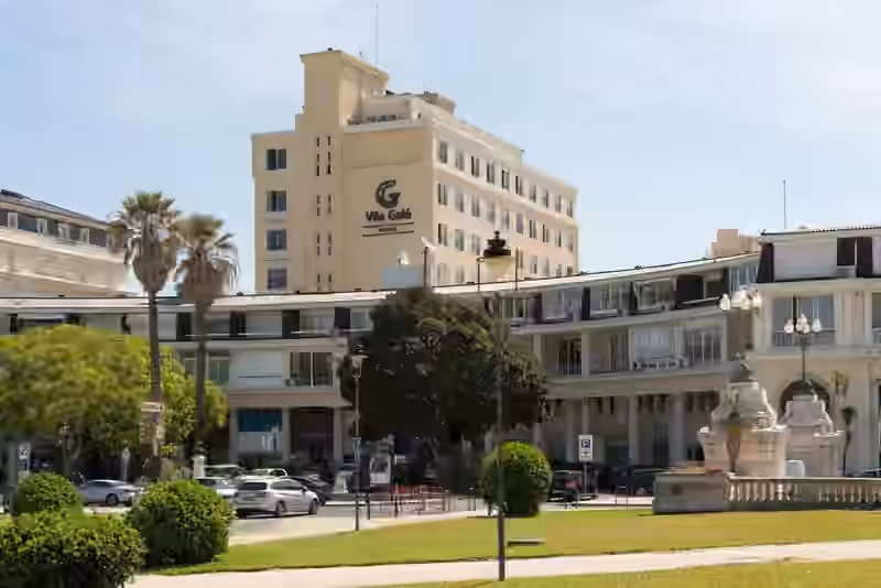Vila Galé Estoril, a cream-coloured hotel block with the Vila Galé logo, rising behind a curved arcade building and palm trees