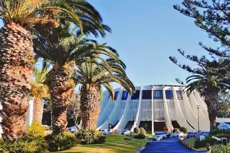 Casino da Madeira, a round white building with curved concrete ribs, seen along its driveway between palm trees