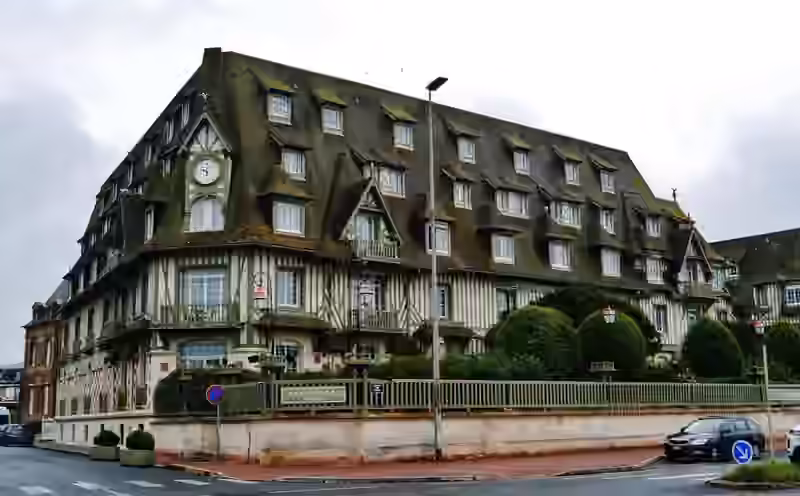 Corner view of Hôtel Barrière Le Normandy in Deauville, with green half-timbering, a clock gable and moss-covered roofs