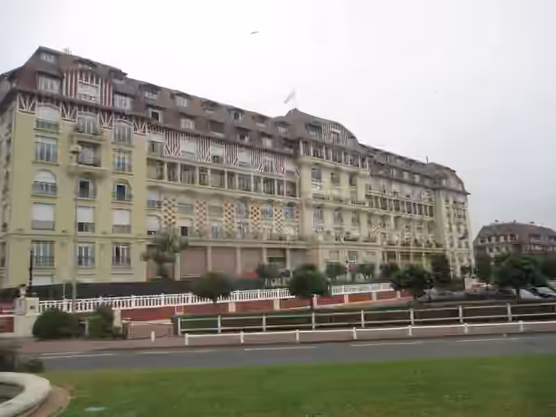 The long main facade of Le Royal hotel in Deauville seen from across the road, with red and white patterned upper floors