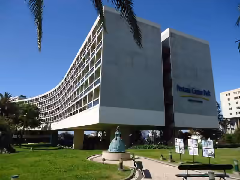 The curved concrete wing of Pestana Casino Park raised on pillars above a lawn, with a statue in front