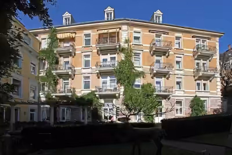 Garden side of the Bad Hotel zum Hirsch in Baden-Baden with balconies on every floor, seen past a stag sculpture