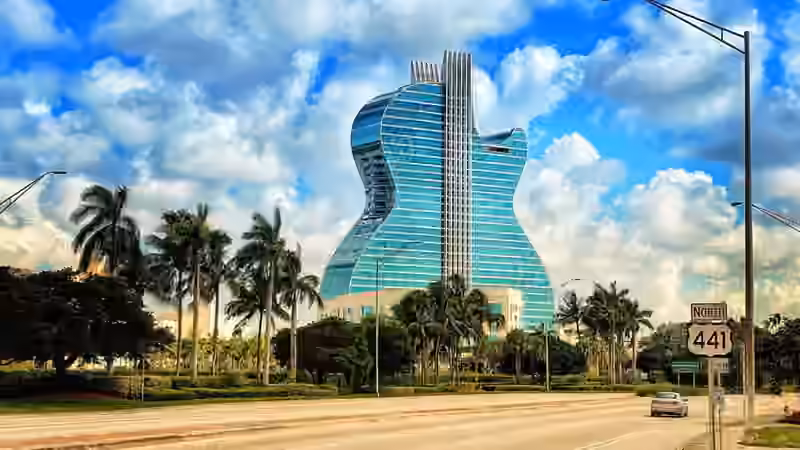 The guitar-shaped glass tower of The Guitar Hotel in Hollywood, Florida, seen from the road behind a row of palm trees
