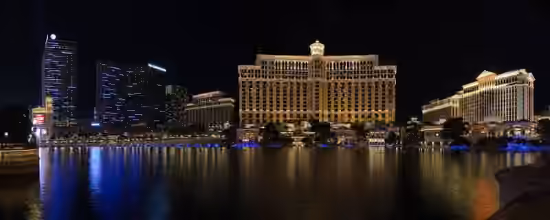Bellagio at night seen across its lake from the Las Vegas Strip, the curved hotel building lit in warm light and reflected in the water