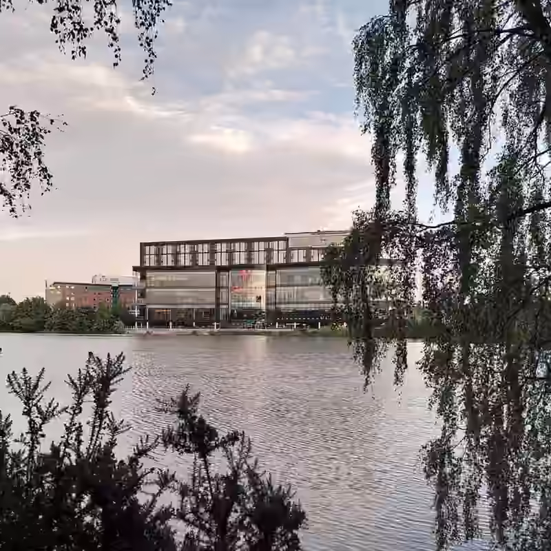 The glass-fronted Resorts World Birmingham building, which houses the Genting Hotel, seen across Pendigo Lake through hanging birch branches