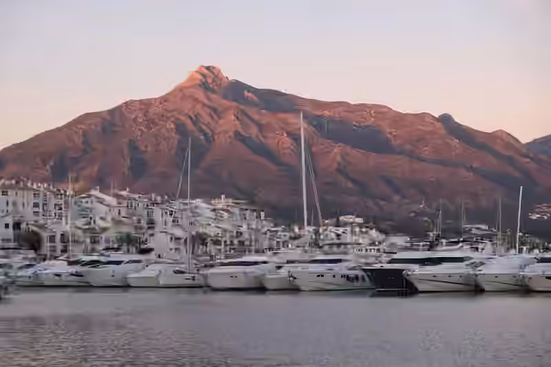 Yachts moored in the Puerto Banús marina in Marbella, with white houses and the Sierra Blanca mountain behind