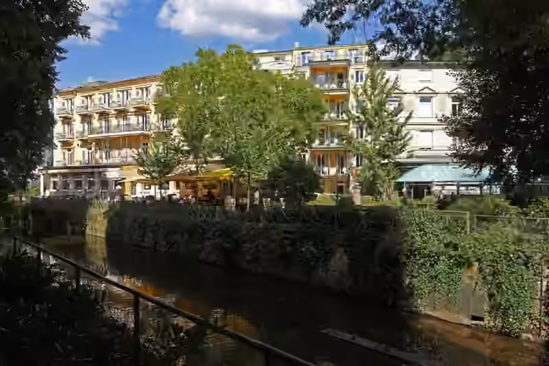 The Atlantic Parkhotel and its terrace seen across the river Oos, behind trees