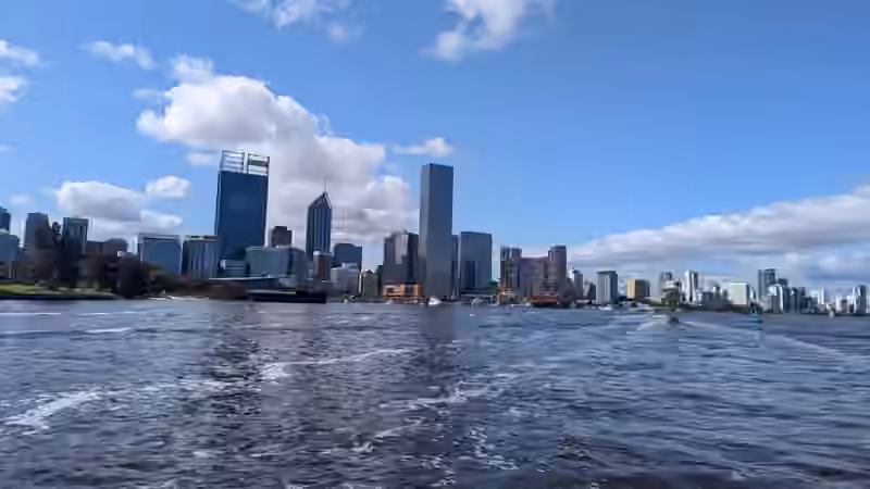 The towers of central Perth seen across the Swan River under a blue sky with white clouds