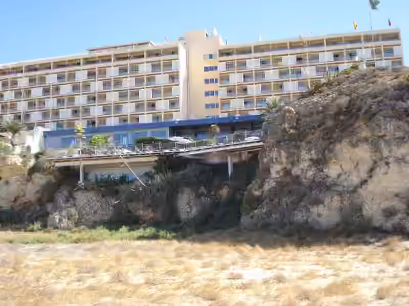 The sea-facing side of Hotel Algarve Casino above the rocks of Praia da Rocha, with rows of balconies and a terrace