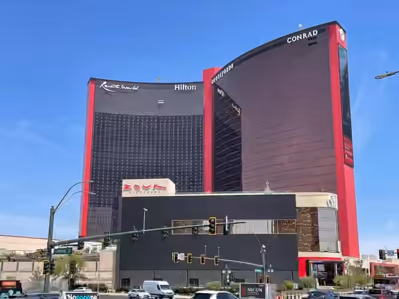 The red and dark glass towers of Resorts World Las Vegas seen from Las Vegas Boulevard, with the Resorts World, Hilton, Crockfords and Conrad signs at the top